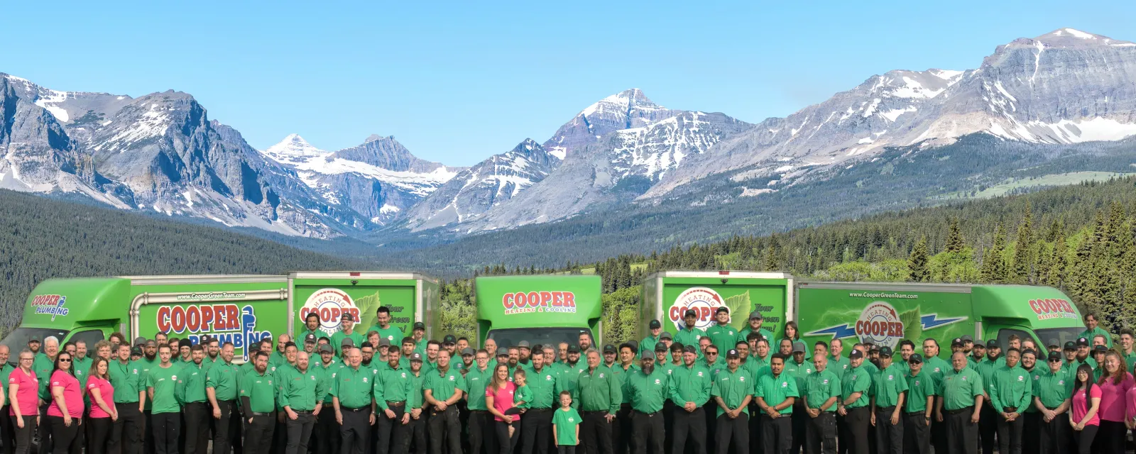 The Cooper Green Team in green uniforms standing in front of their service trucks with the Rocky Mountains behind them